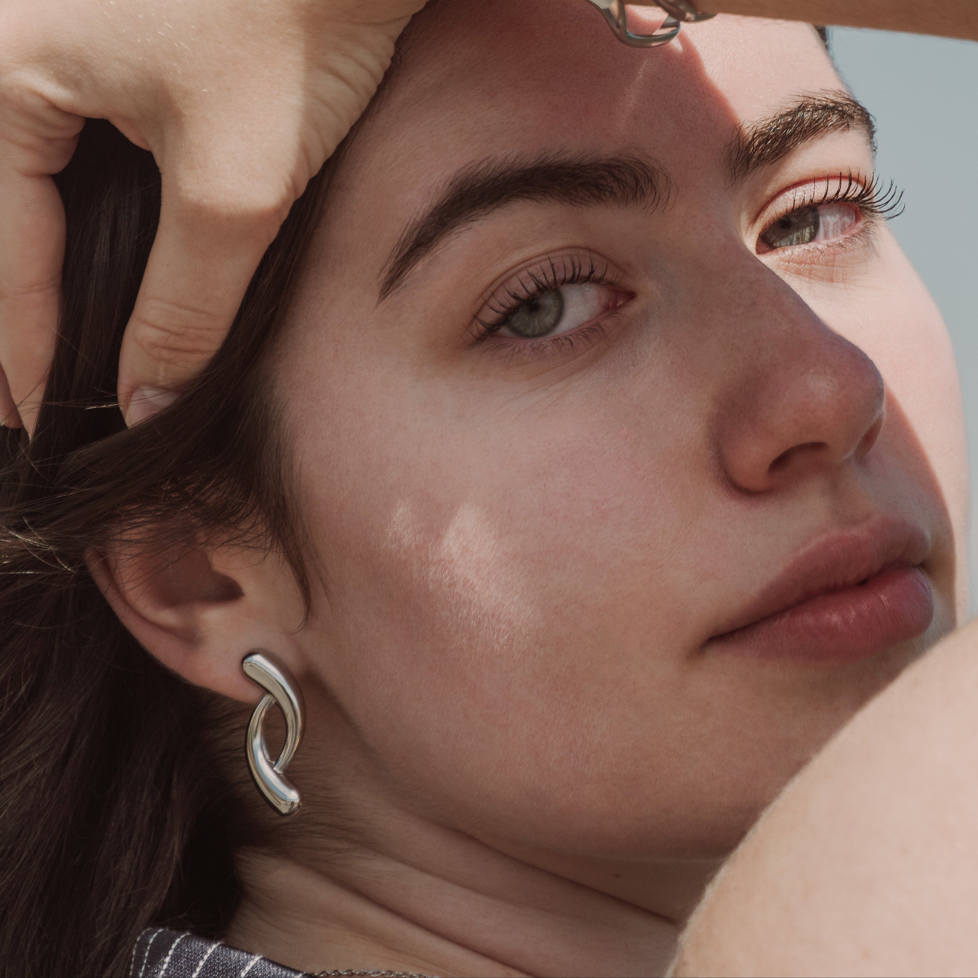 Close-up of a person wearing silver hoop earrings and a bracelet against a blurred background